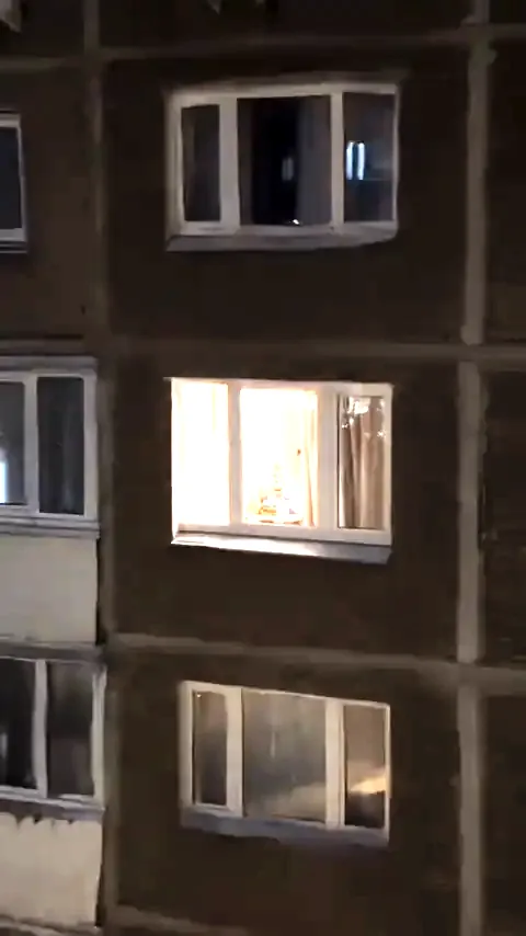 A diner paused mid-bite inside a warm apartment window at night